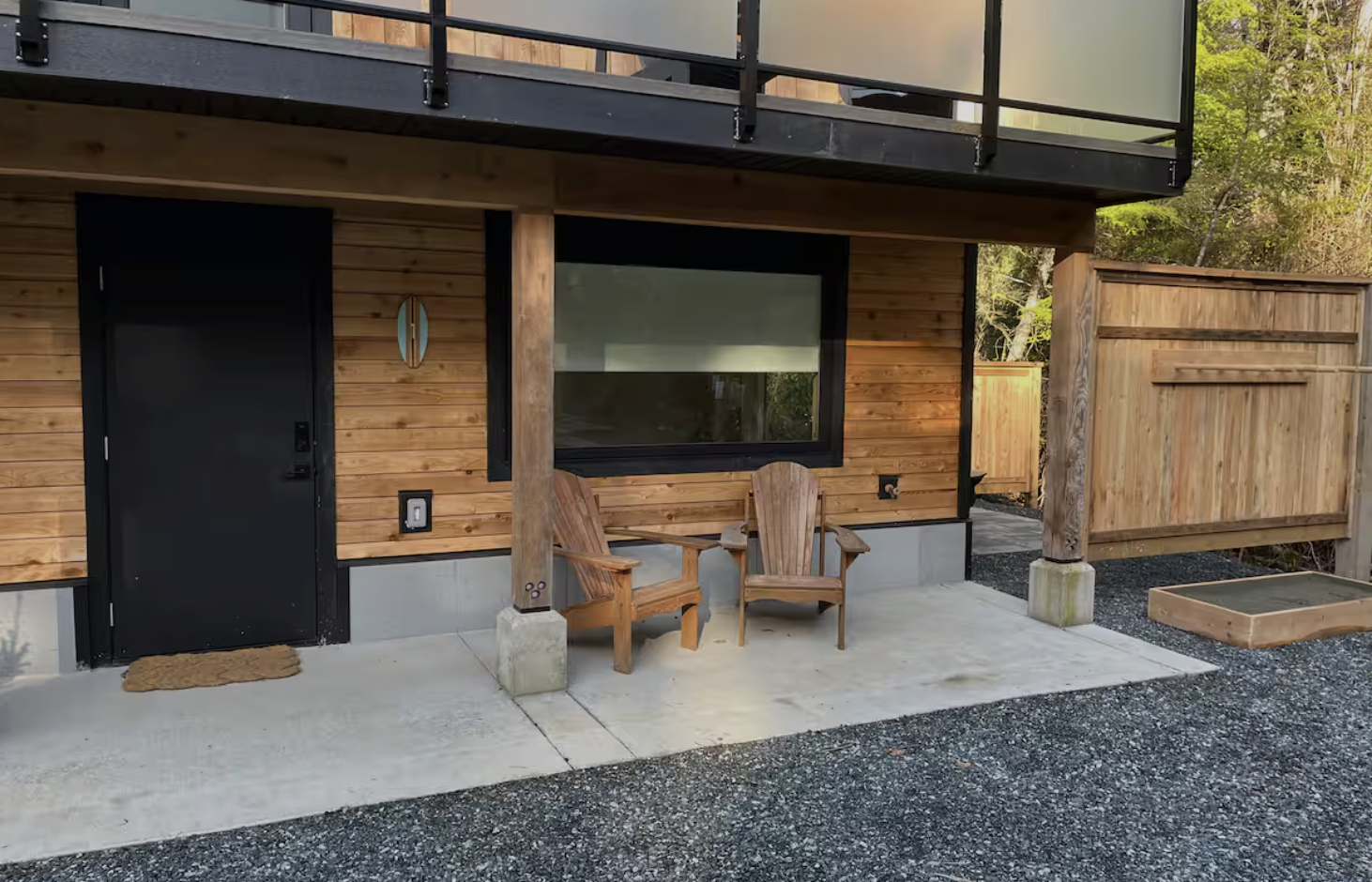 Front porch of a modern wooden house with black door, window, and two wooden chairs