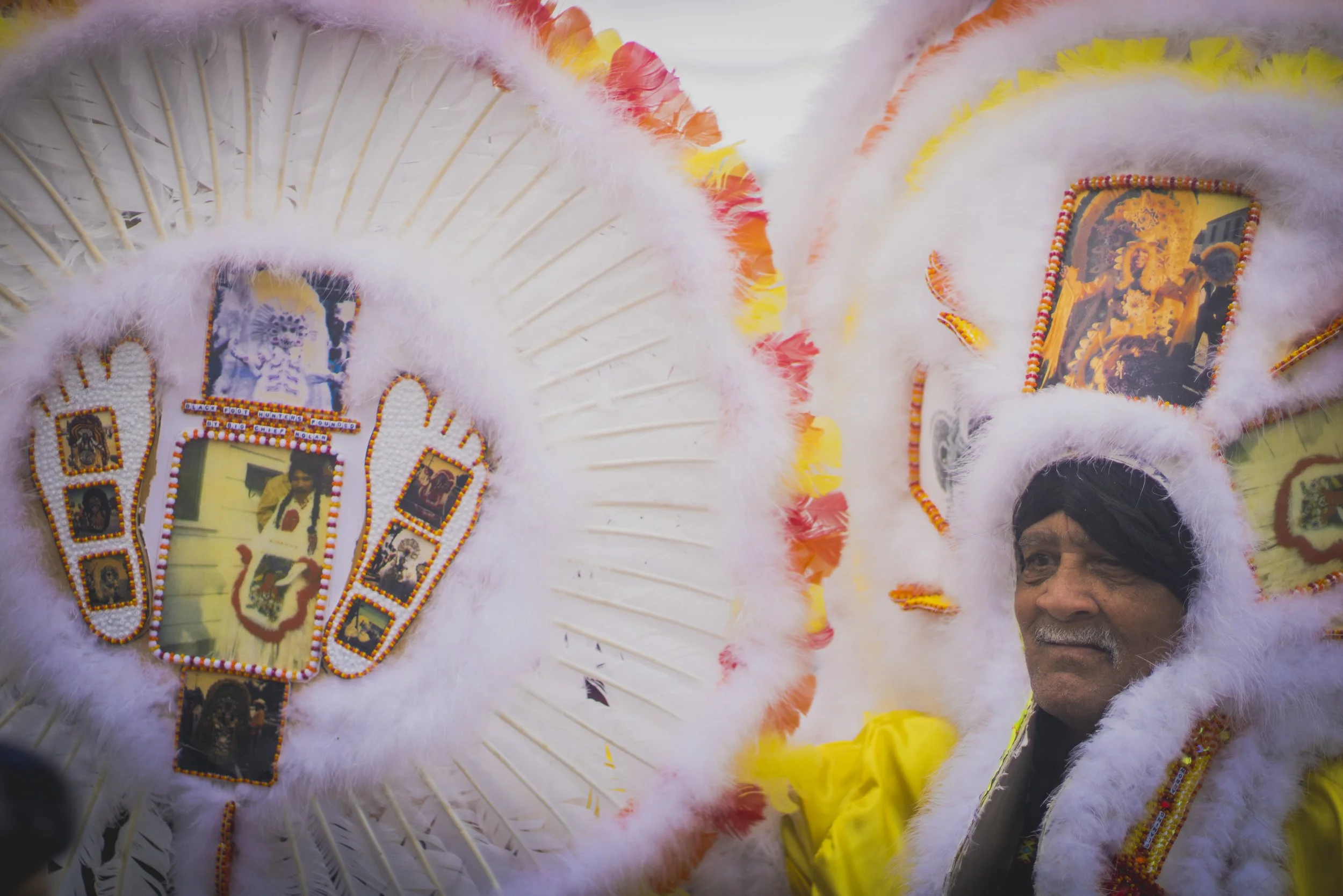 Close-up of a person wearing a colorful feathered headdress decorated with photos and beads, likely part of a traditional or cultural celebration.