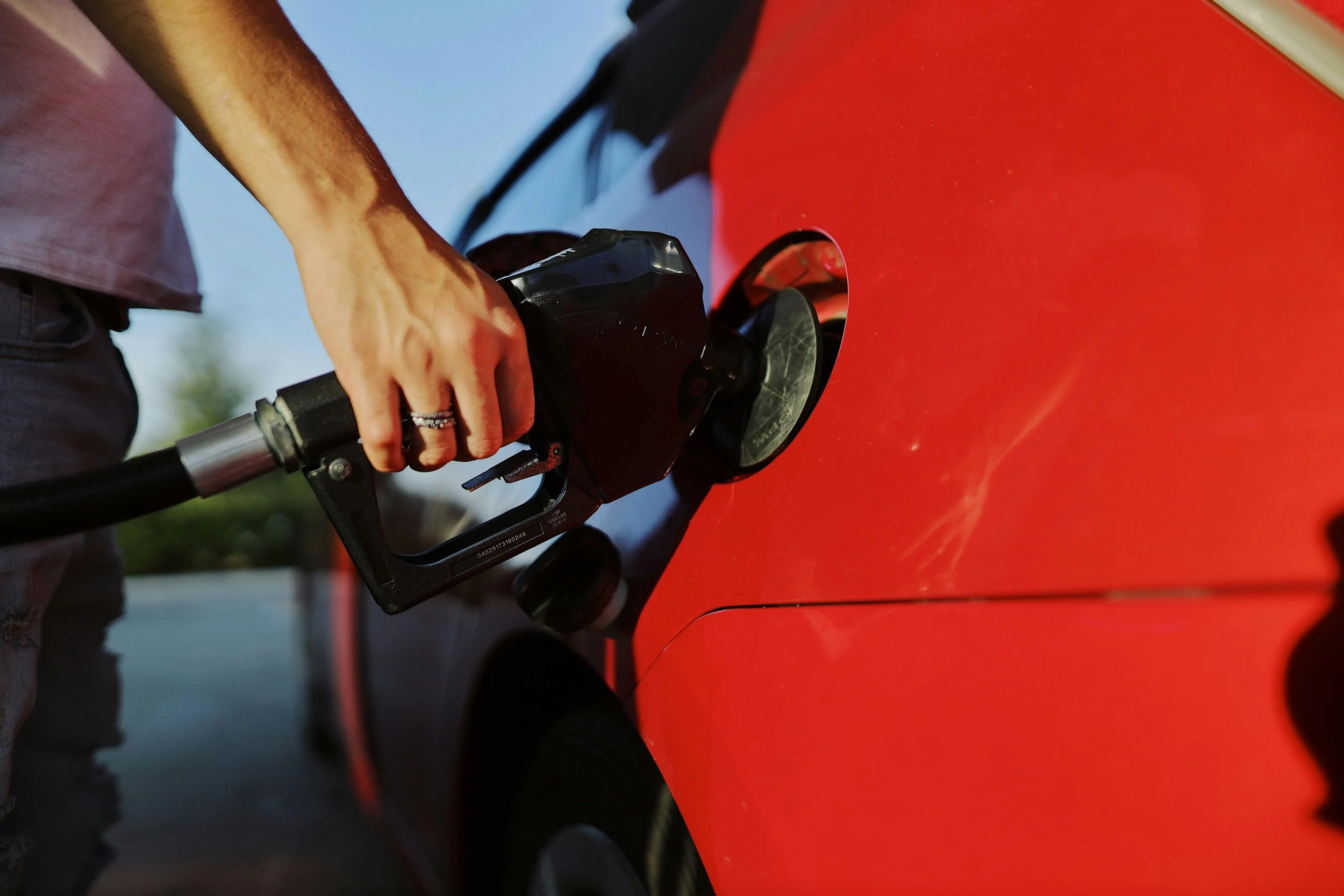 Person refueling a red car at a gas station.