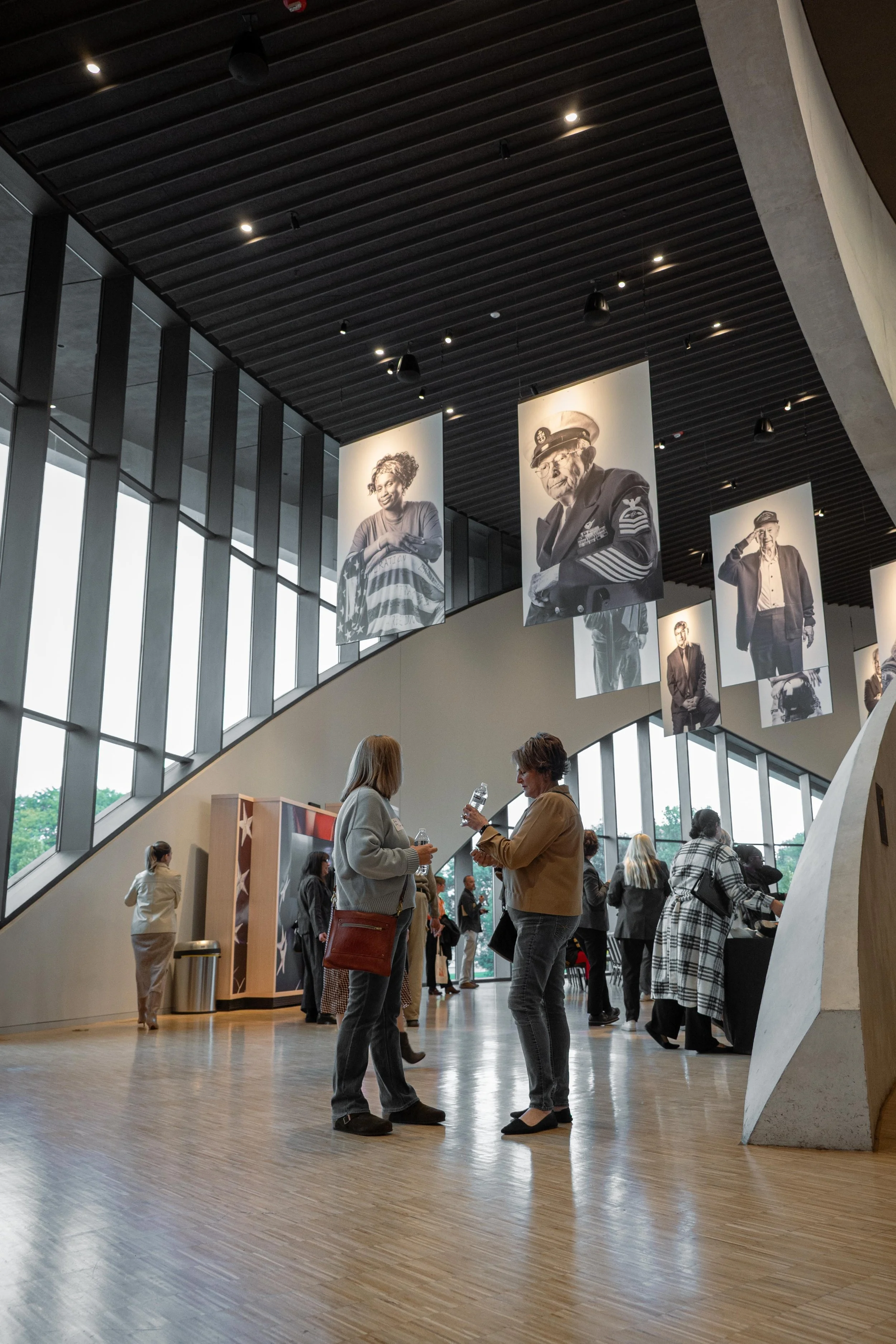 People gathered inside a modern building with large windows and black banners displaying black and white portraits of diverse individuals.