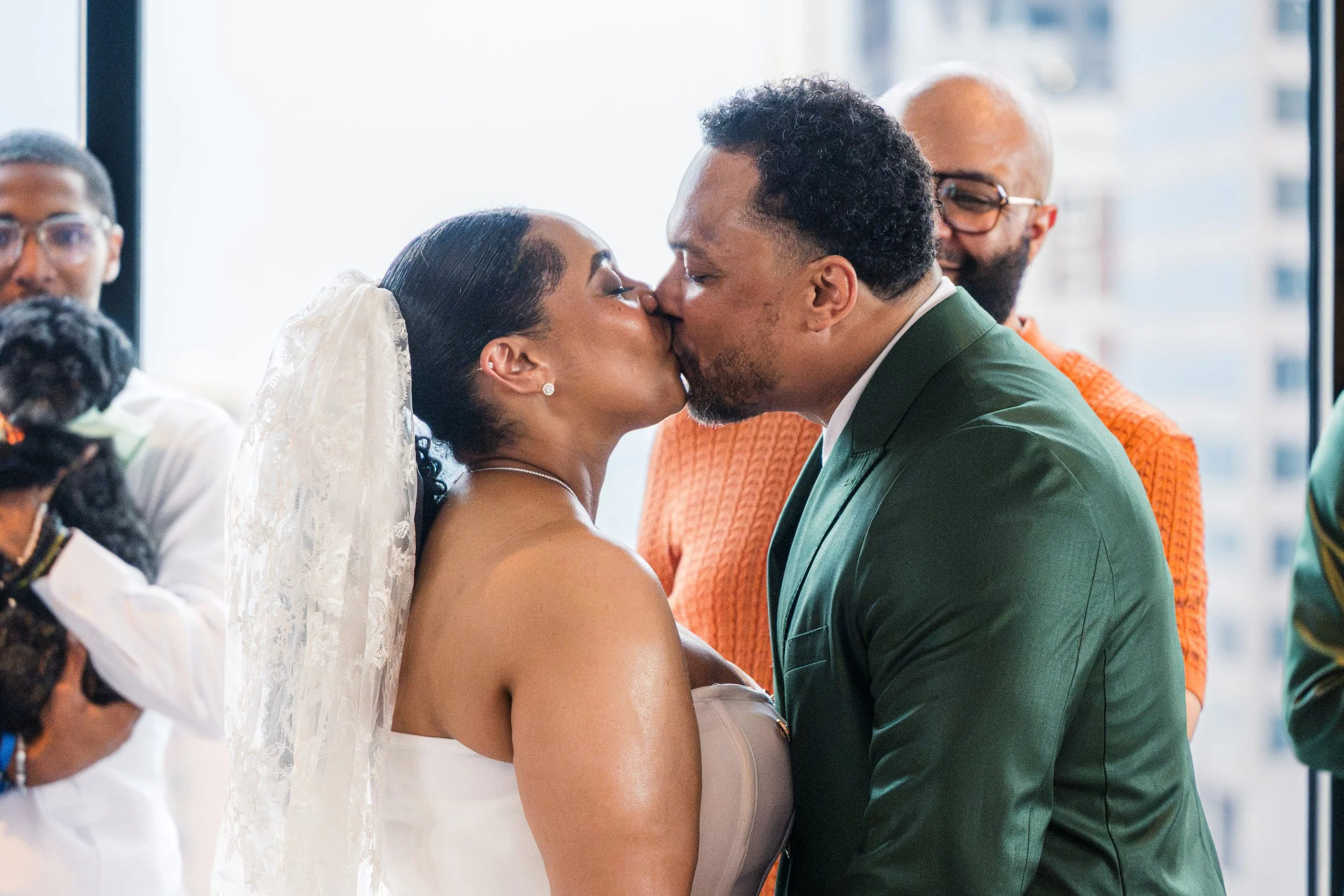 A couple is kissing each other during their wedding ceremony, surrounded by friends and family.