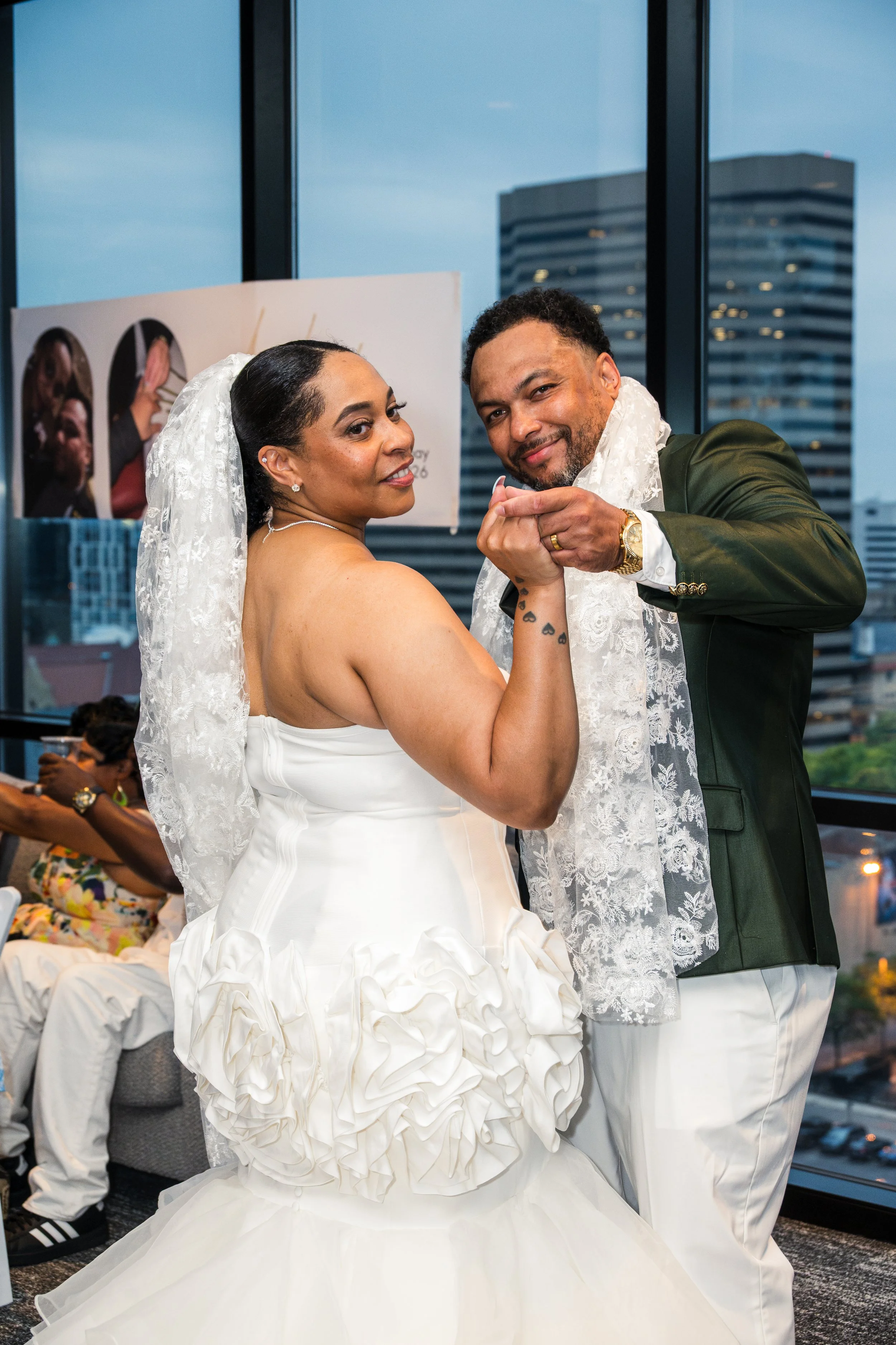 A couple dancing at a wedding reception, with the woman in a white wedding dress and the man in a dark green blazer, both holding hands and smiling.