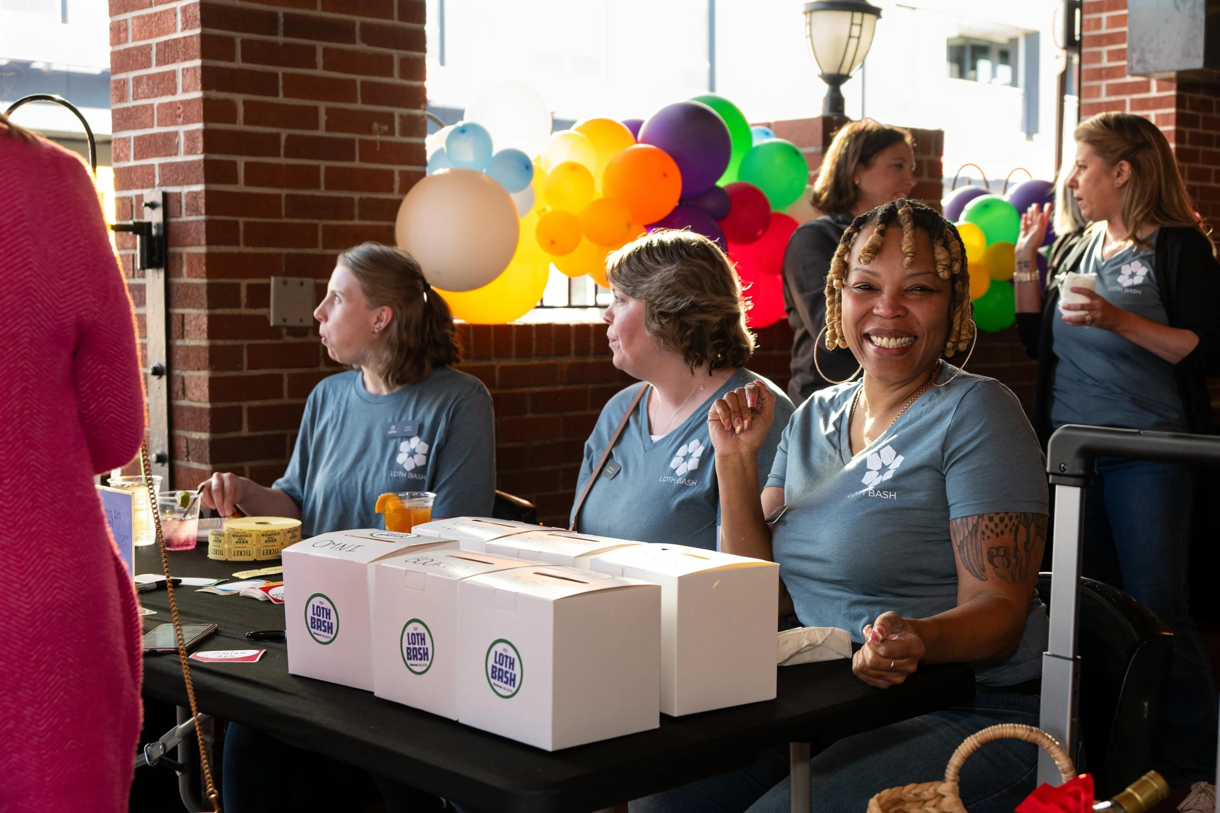 Smiling woman with braided hair sitting at table with boxes and colorful balloons behind her