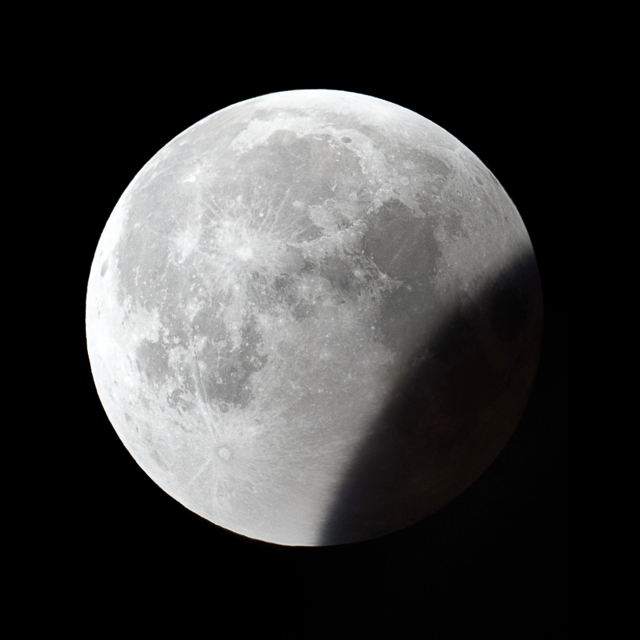 Close-up image of the full moon with a shadow cast on its right side against a black night sky.