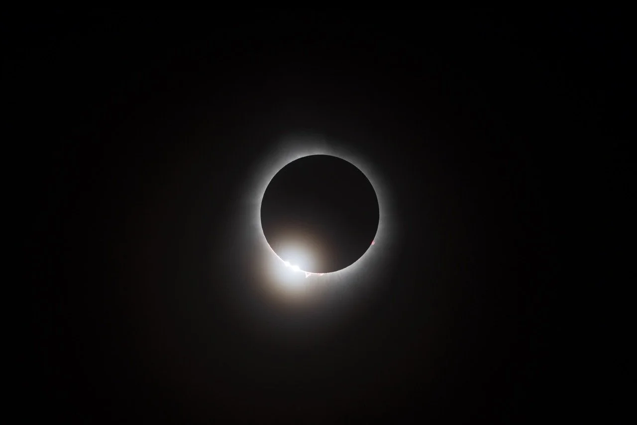 A solar eclipse with the moon blocking the sun, creating a dark circle surrounded by a glowing white corona.