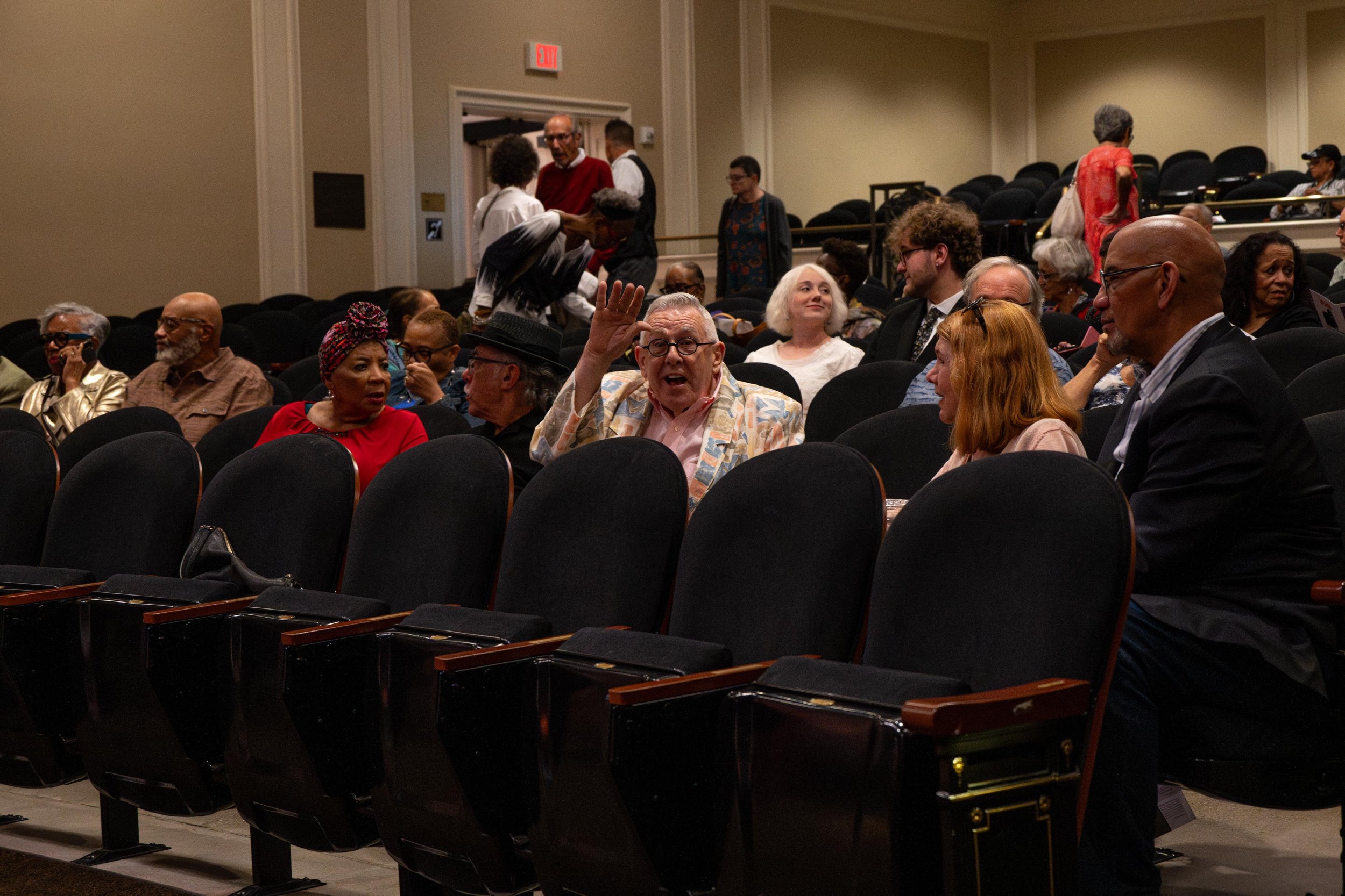 People seated and standing in a lecture hall or auditorium, engaged in conversation and waiting for an event to start.