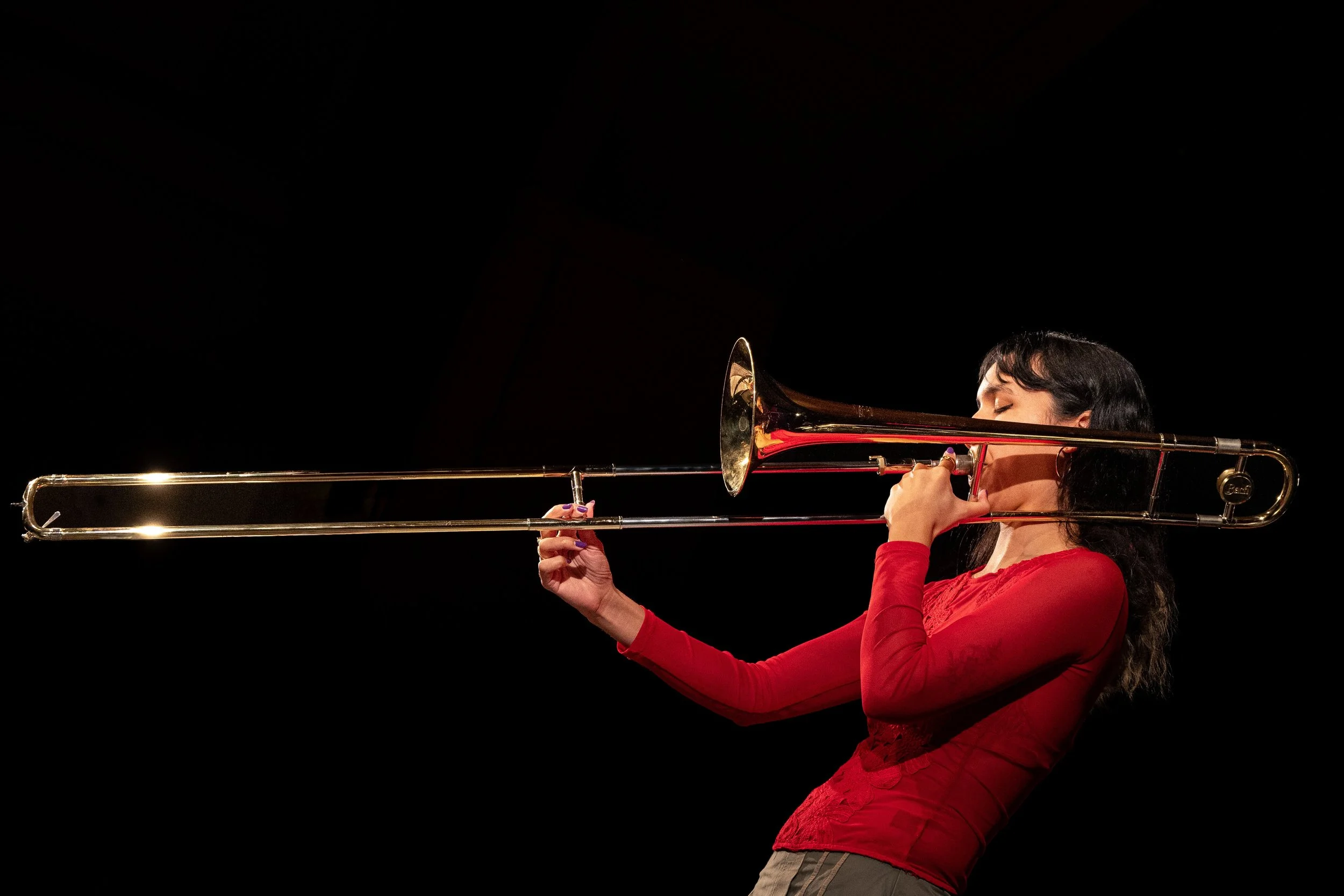A woman in a red dress playing a trombone against a black background.