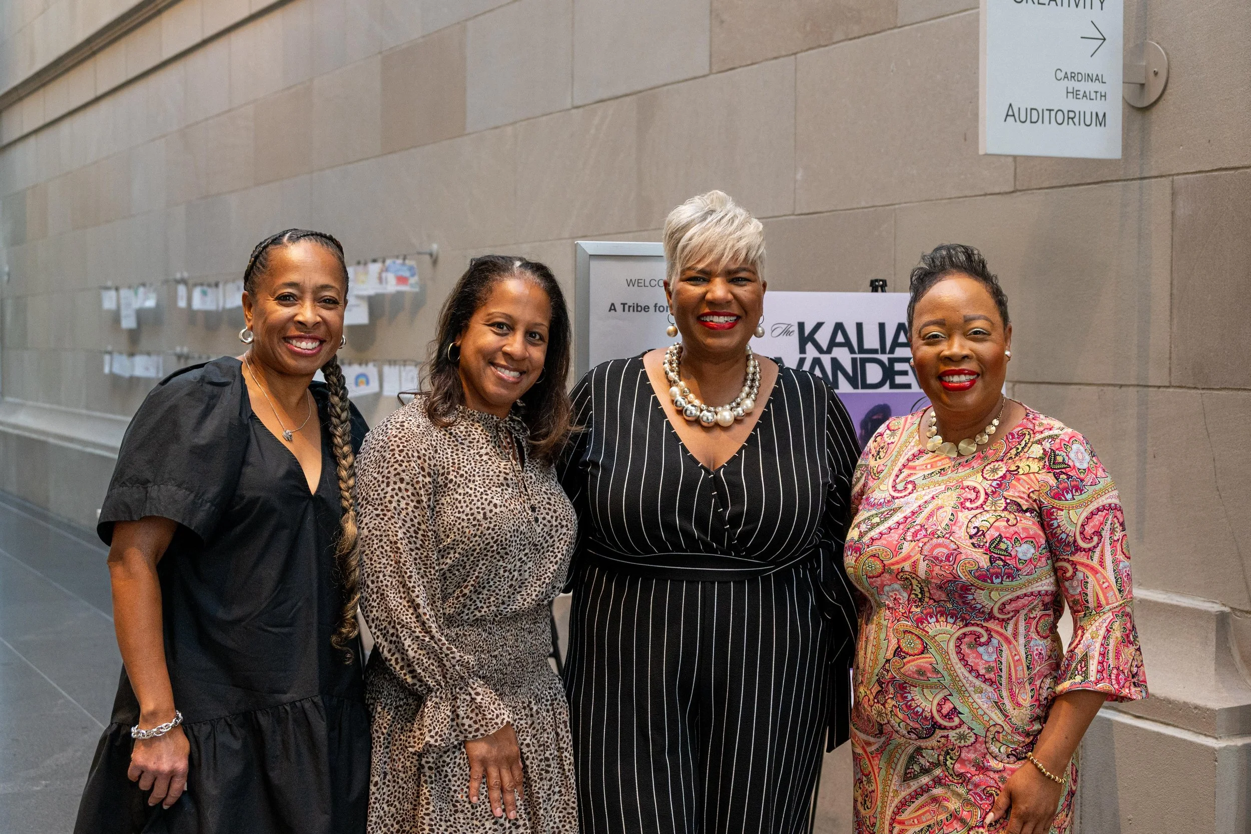 Four women standing together in a hallway, smiling for the camera, in front of a sign that reads 'Cardinal Health Auditorium.'