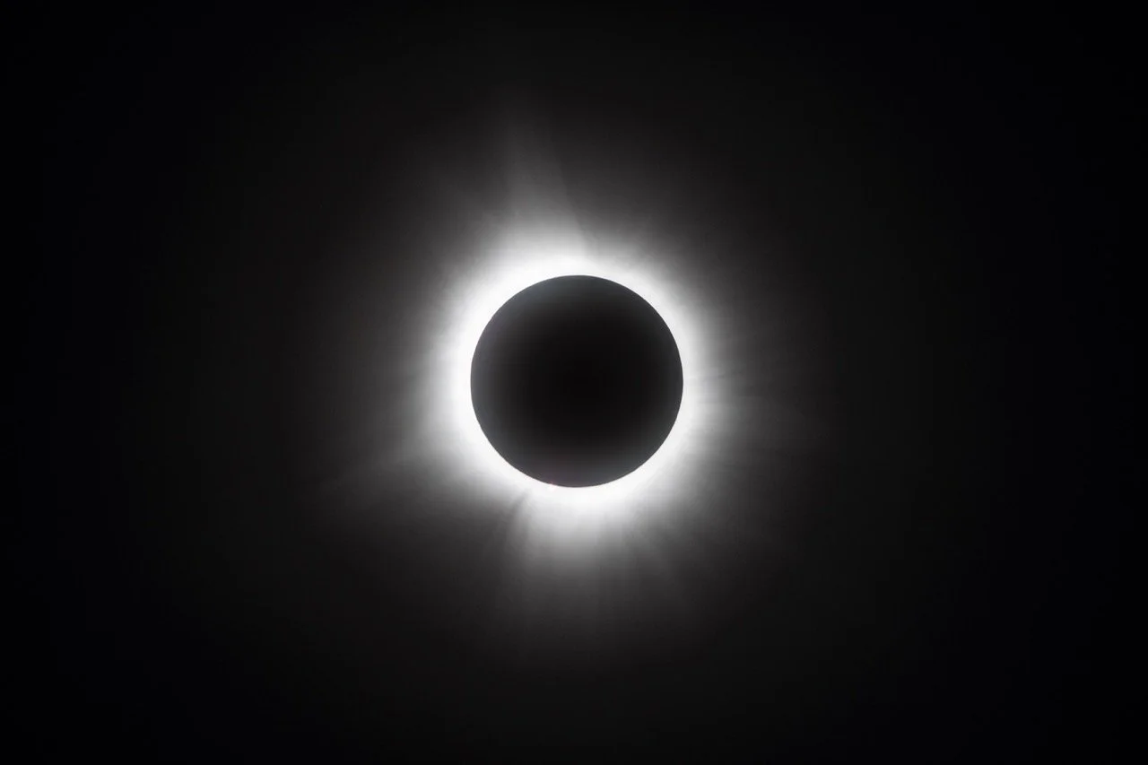 A solar eclipse with the moon covering the sun, creating a dark circle surrounded by a bright halo of light.