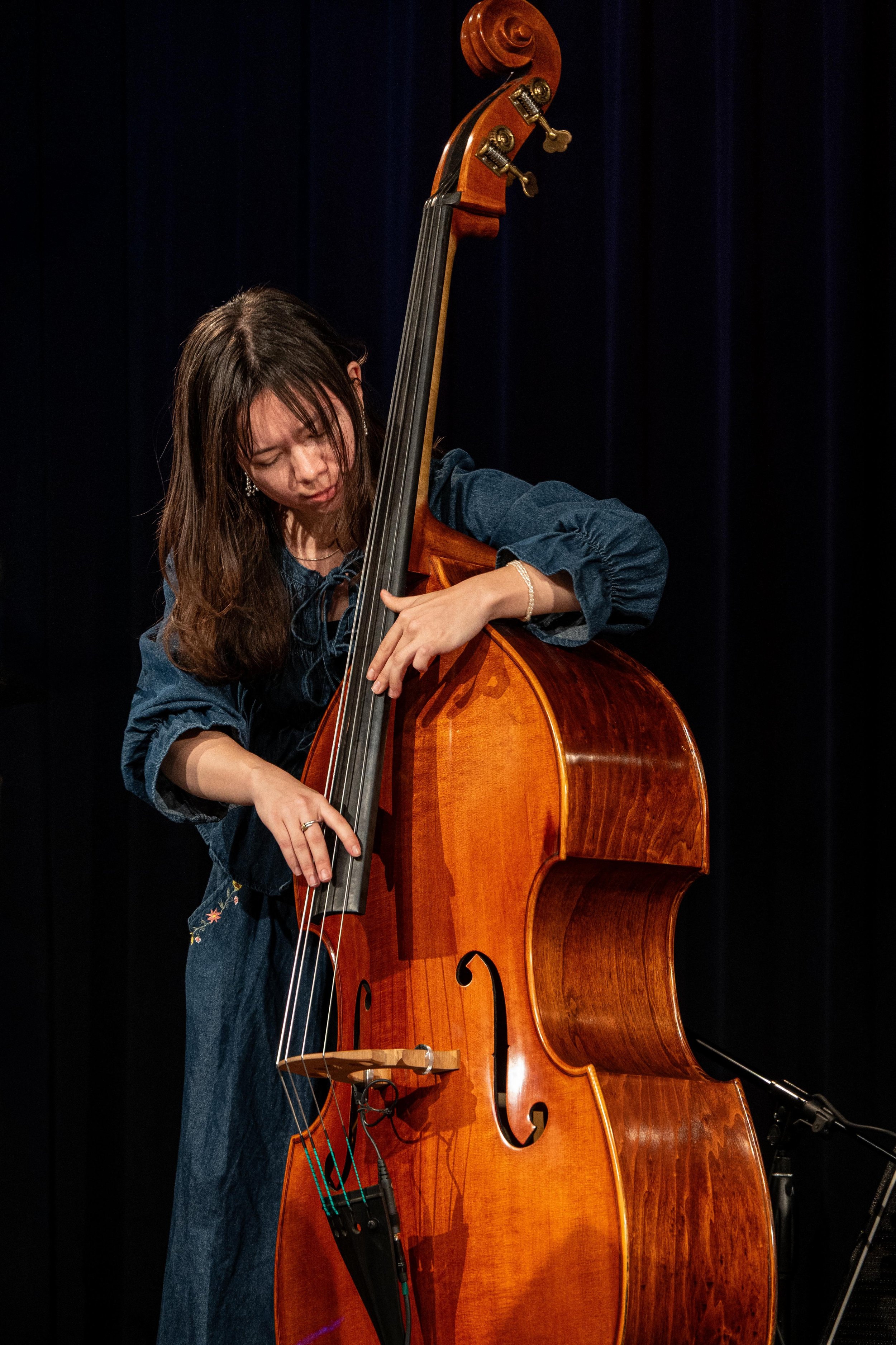 Woman playing a double bass on stage, with a dark background.