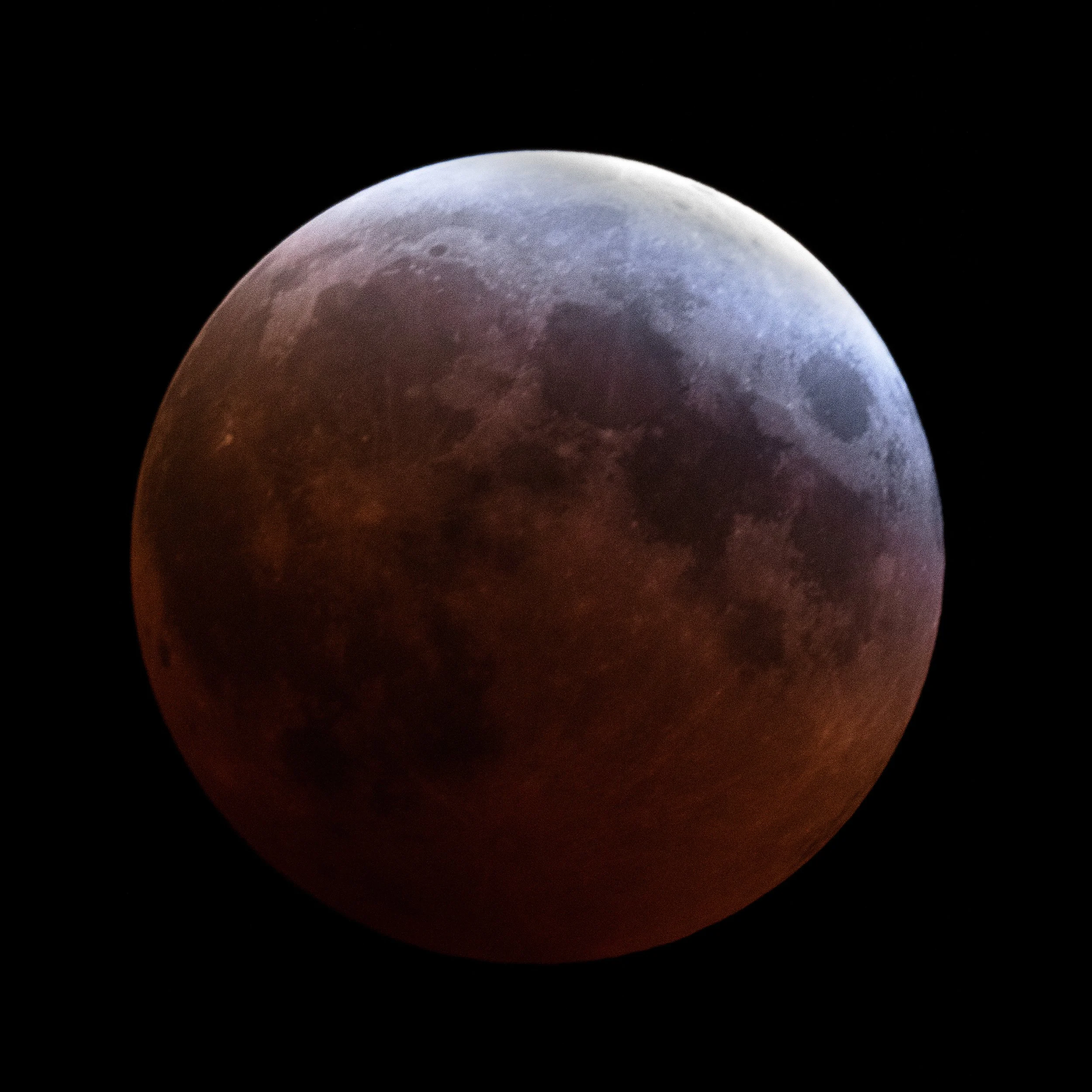 Close-up of a lunar eclipse showing the moon partially covered by Earth's shadow against a black sky.
