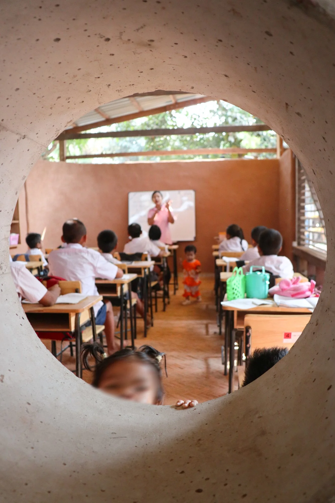 Ein Klassenzimmer mit Schülern, die an Tischen sitzen, und einer Lehrerin, die vor einer Tafel steht.