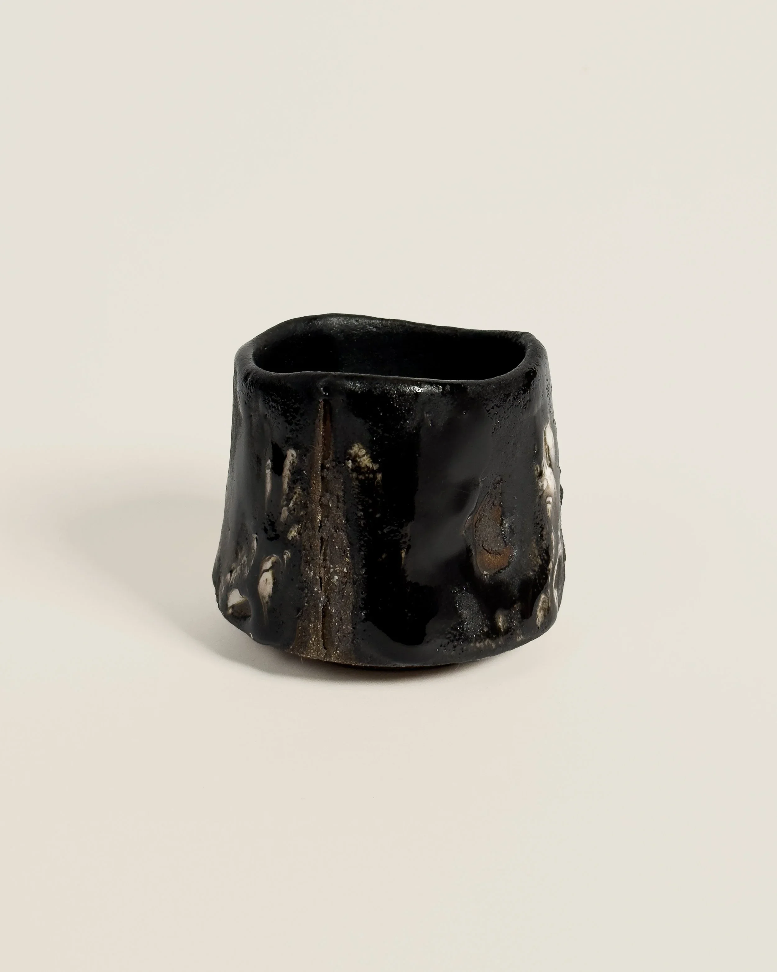 A black ceramic cup with a textured surface and irregular shape, positioned on a plain white background.