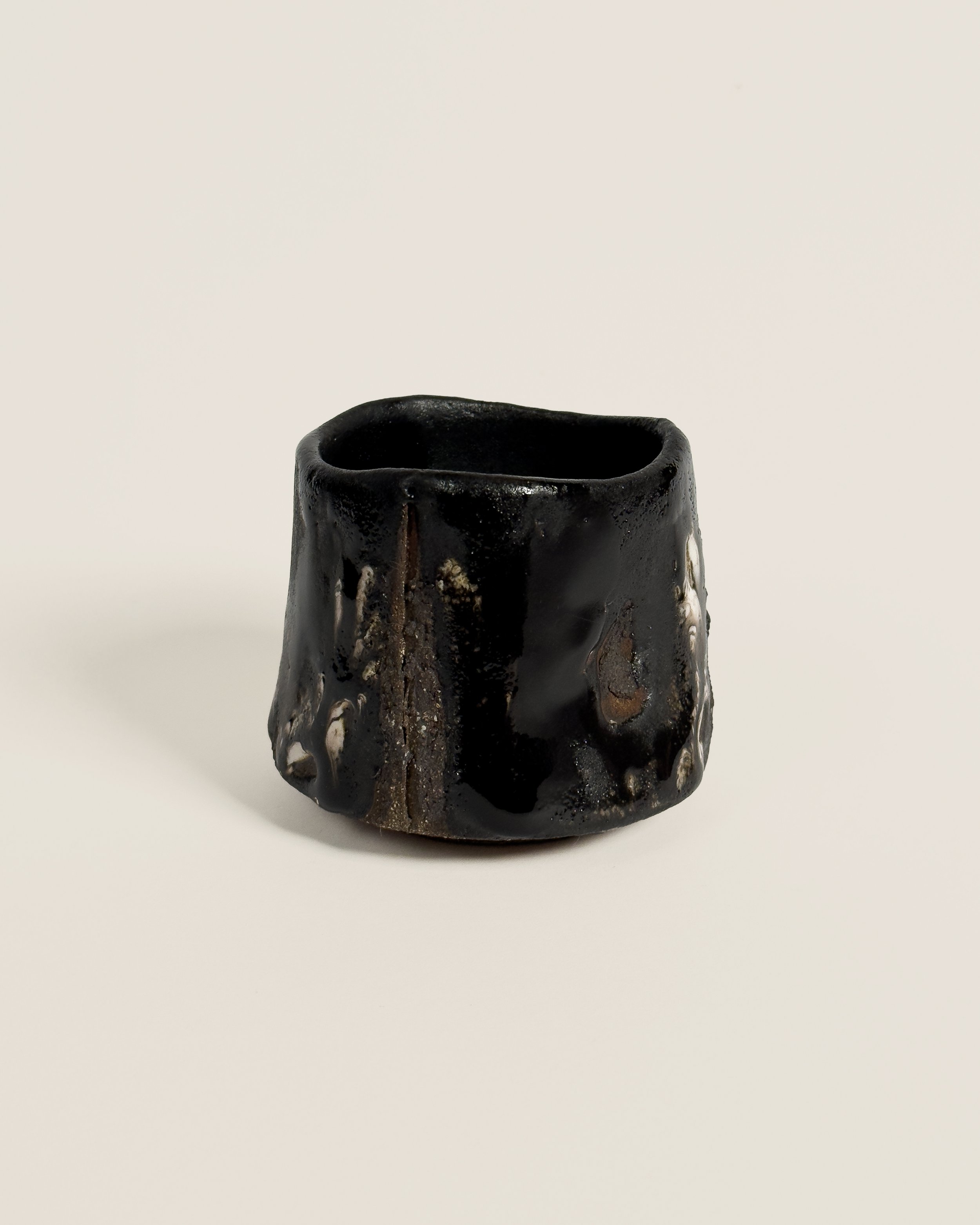 A black ceramic cup with a textured, uneven surface and irregular shape on a plain white background.