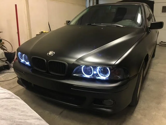 Black BMW sedan with aftermarket halo headlights parked in a garage.