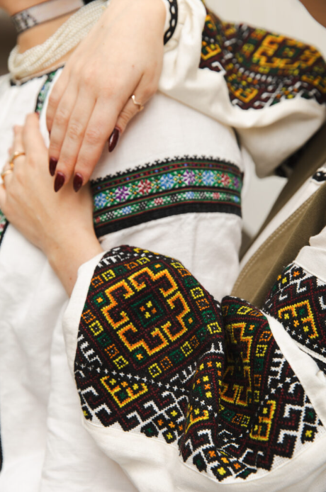 a close up of two beautifully and colourfully embroidered blouses with 2 hands in frame