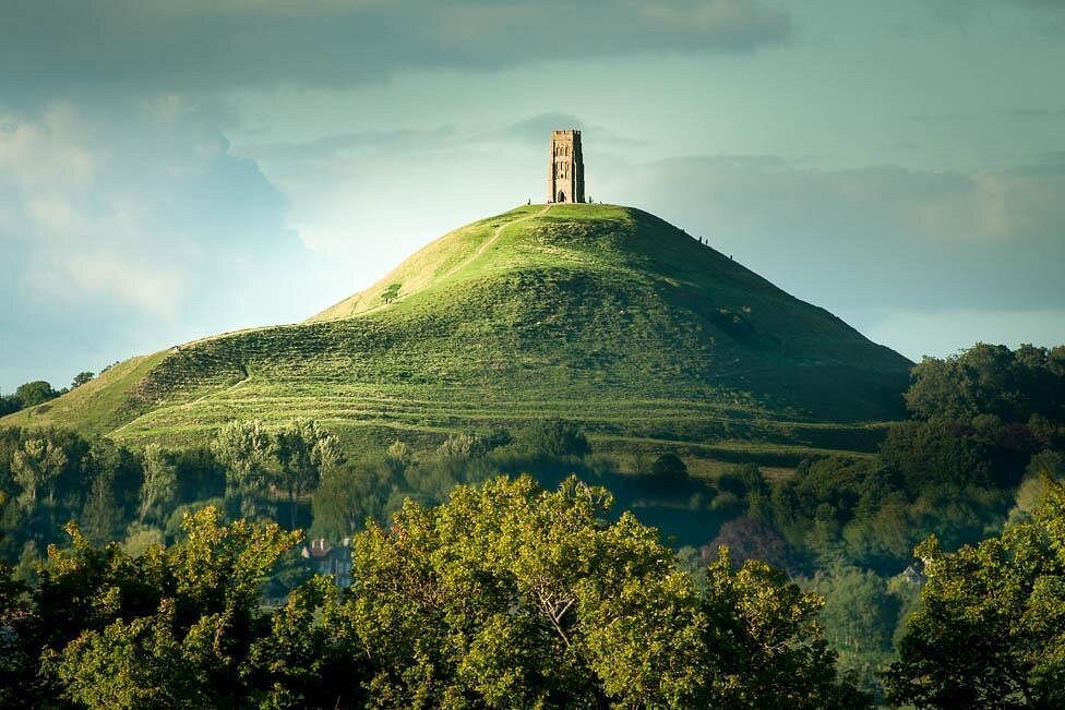 A hill with terraced slopes topped by a tower-like structure, surrounded by trees and greenery.