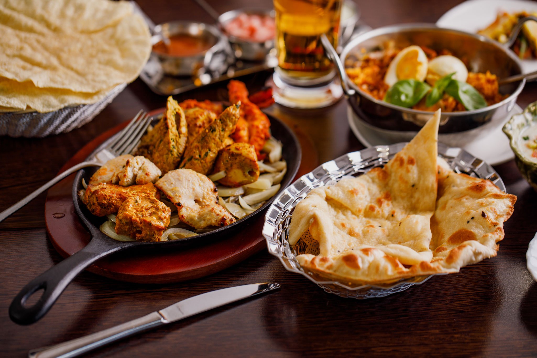 Indian meal with naan bread, chicken tikka, and vegetable dishes on a dark wooden table.