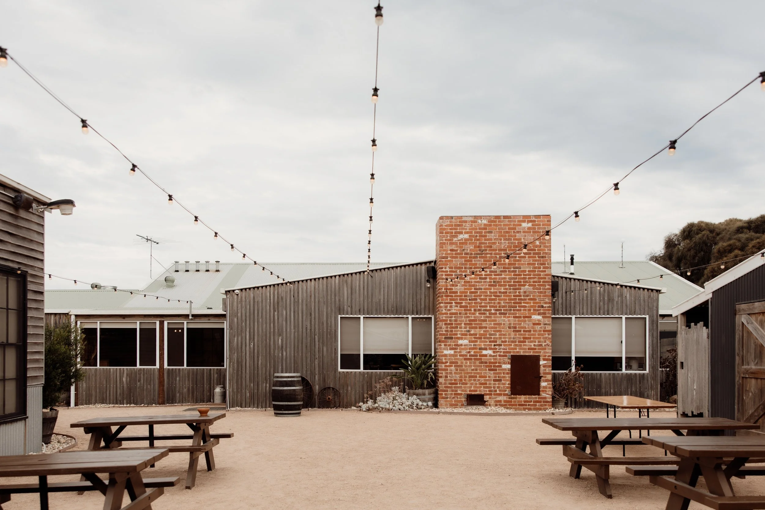 The Shearing Shed as seen from The Courtyard - red brick fireplace, silver timber, tuscan stone, table, festoon lighting. Stunning.