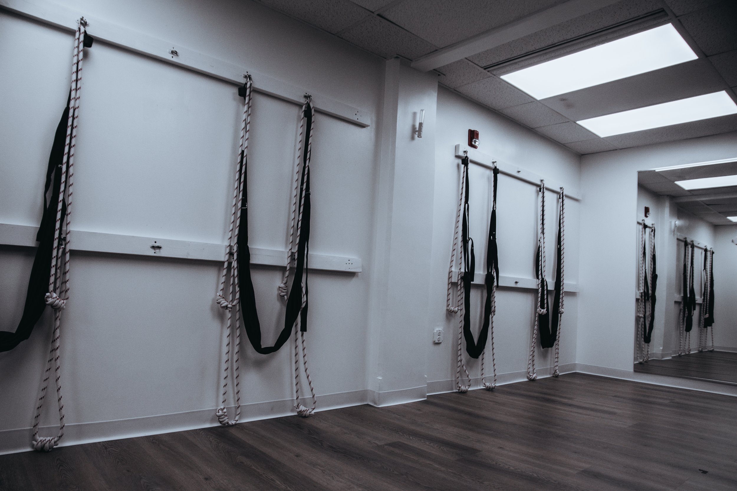 Empty exercise room with black and white ropes hanging on the wall, wooden floor, and ceiling lights.