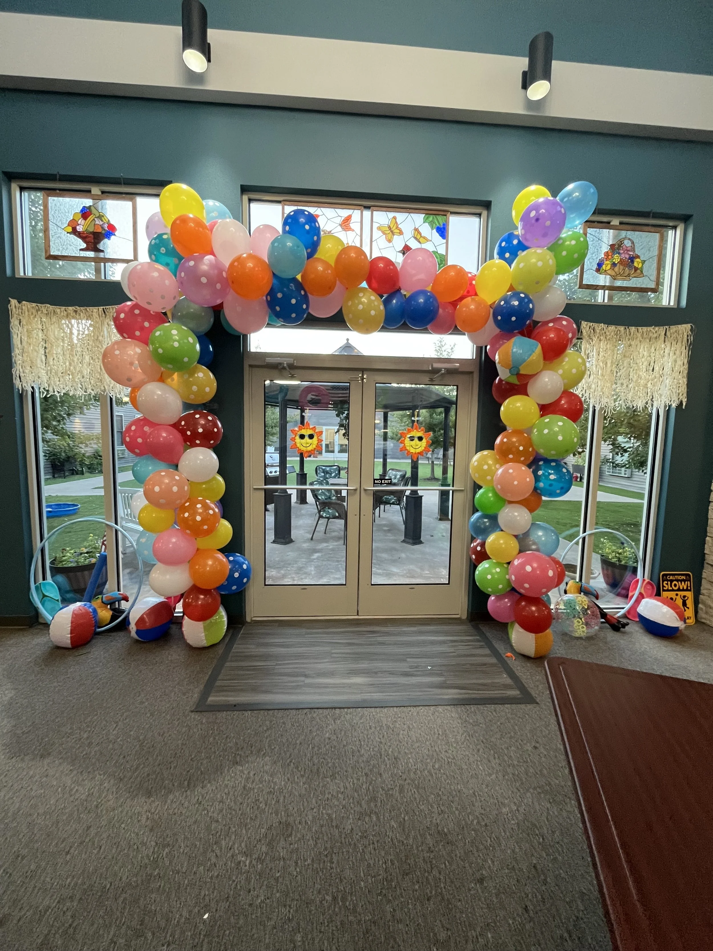 Colorful balloon arch over glass double doors at entrance of indoor space decorated for a celebration or party.
