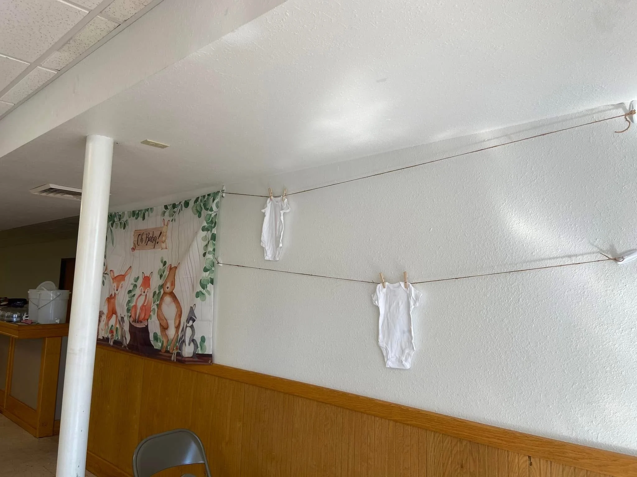 A wall with a string of cloth diapers hanging on it, secured with clothespins. There is a decorative curtain with animals and greenery in the background.