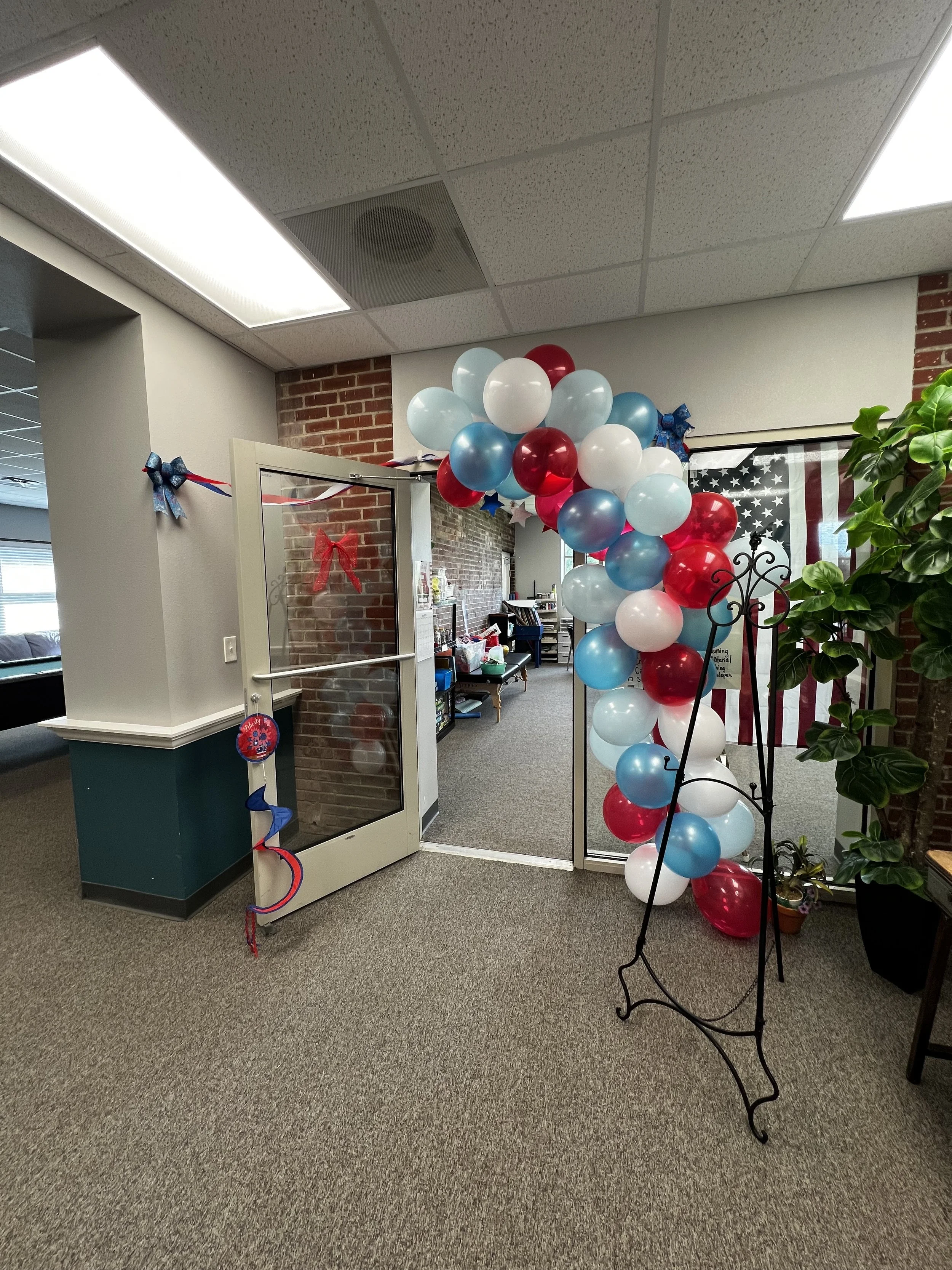 Decorated office entrance with patriotic balloons in red, white, and blue, along with a large American flag poster in the background.