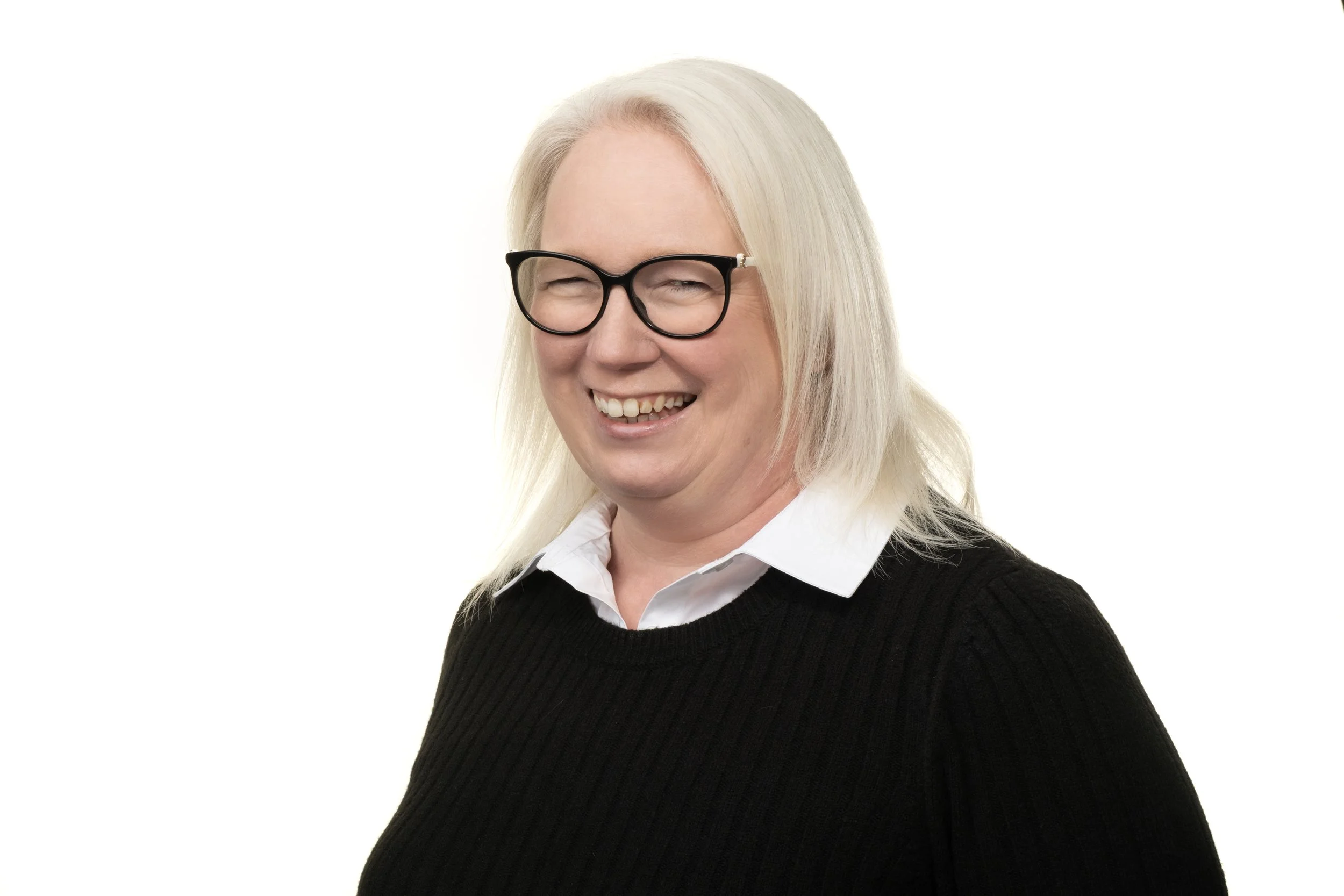 A woman with blonde hair, black glasses, smiling, wearing a white shirt and black sweater, against a white background.