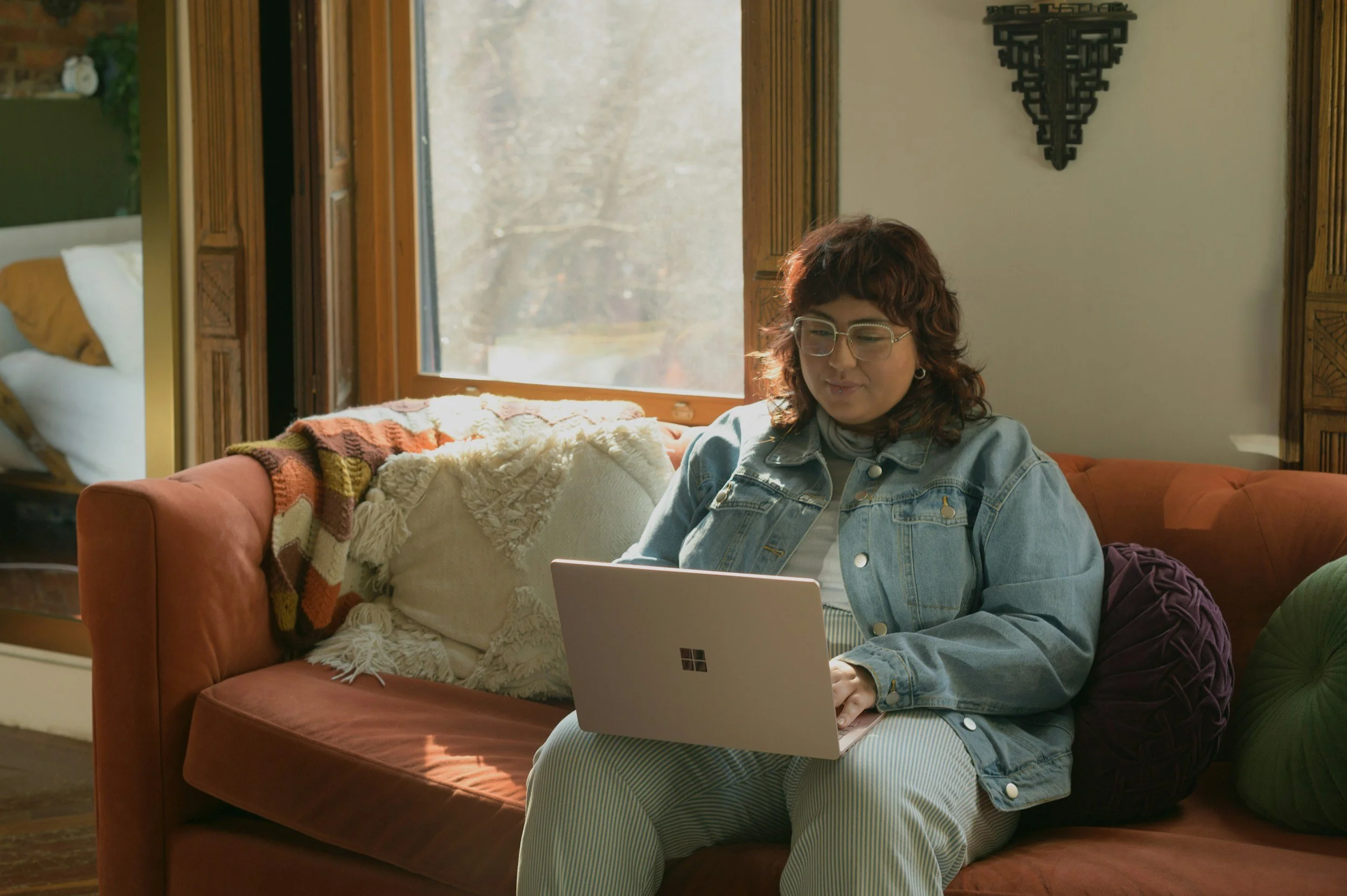 Photo of a person seated on a couch using a laptop, in a relaxed, home-like settingm, representing accessible telehealth occupational therapy
