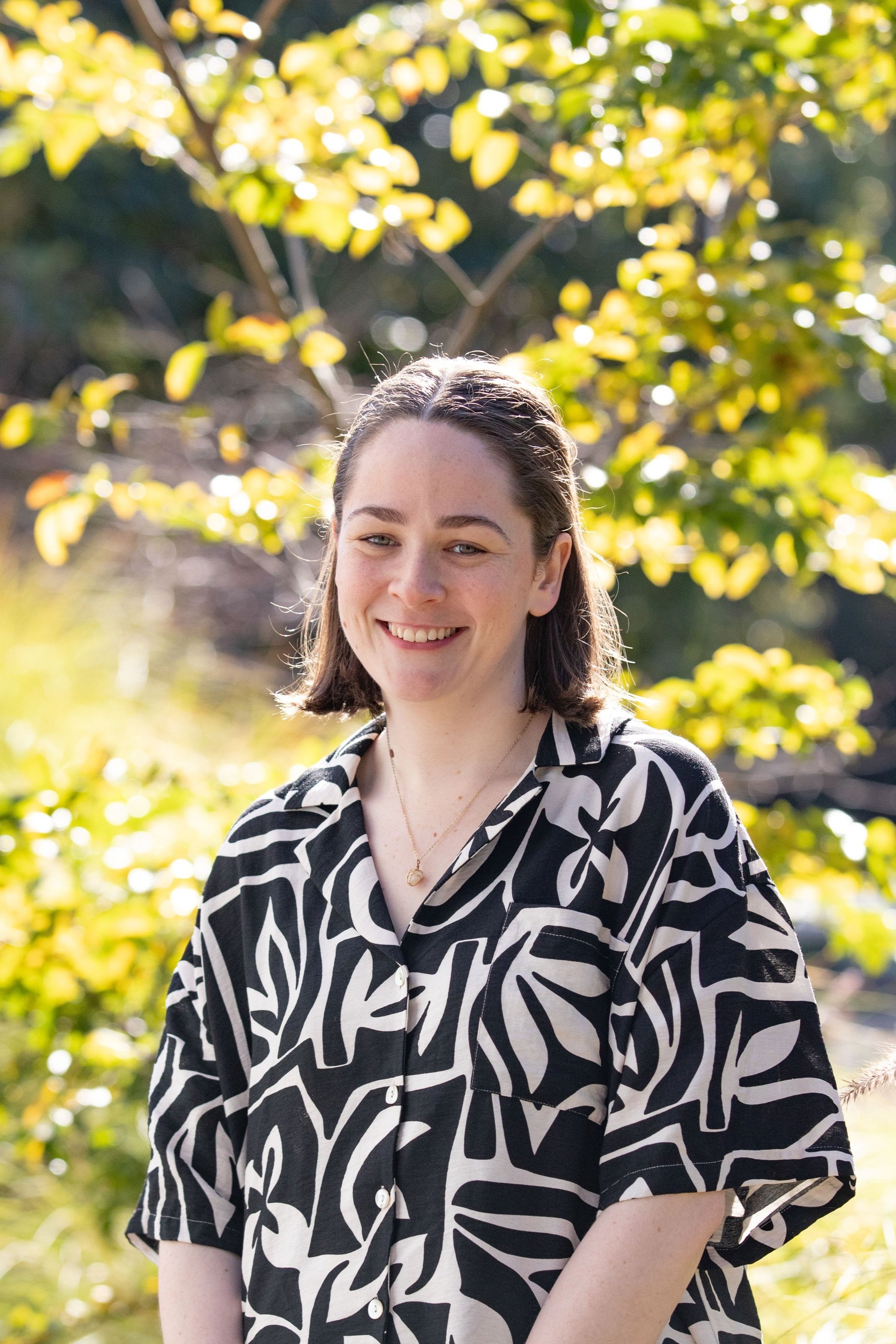 Portrait of Martha Kennedy, neurodivergent-affirming occupational therapist, smiling outdoors in front of trees