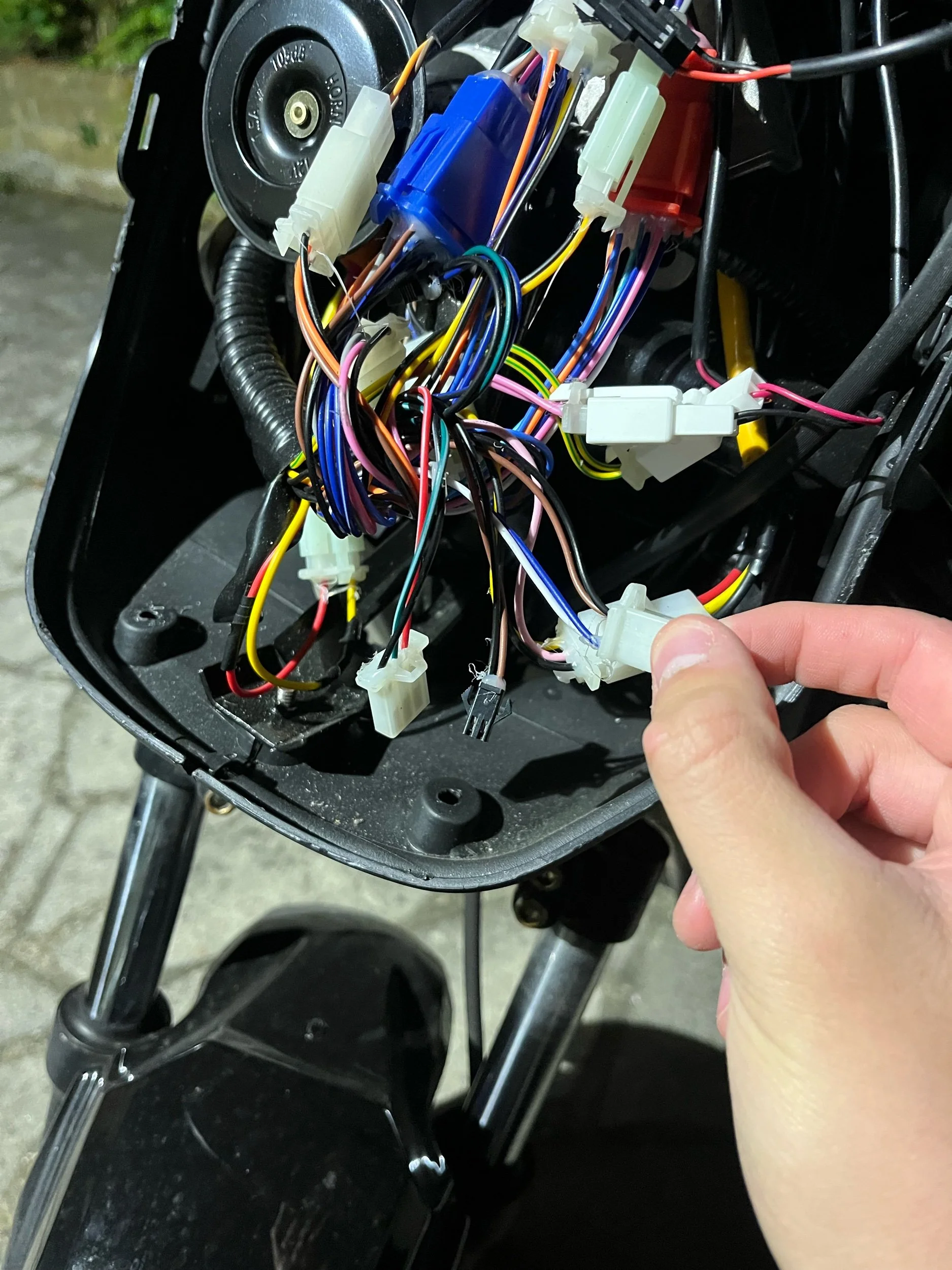 Close-up of a motorcycle dashboard with exposed wiring and connectors, with a person's hand holding a connector.