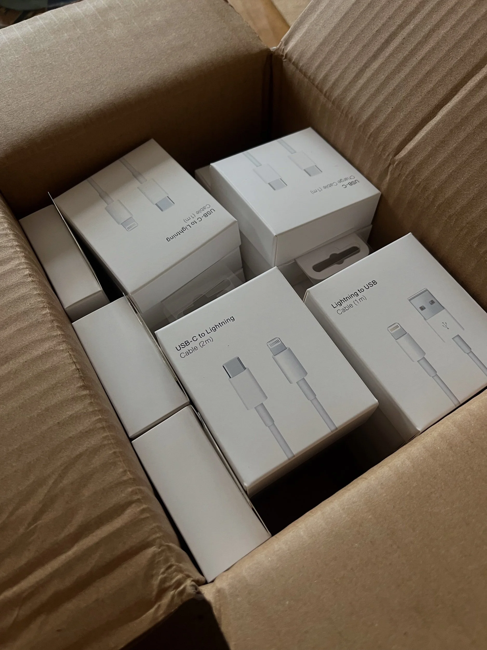 Open cardboard box containing multiple white boxes of USB-C to Lightning cables.