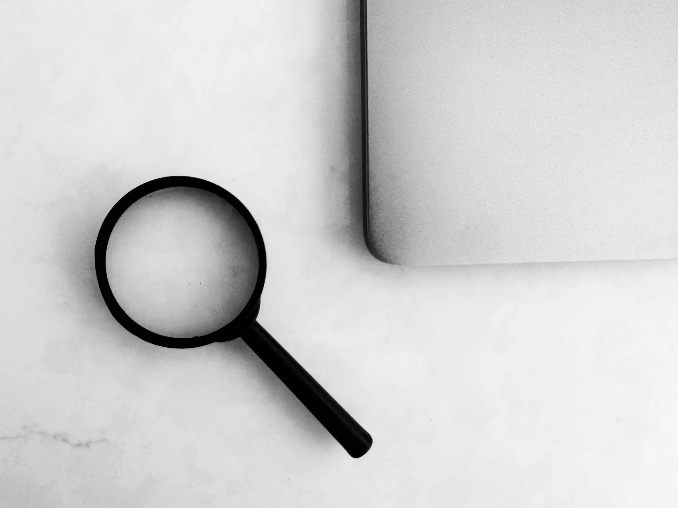 Magnifying glass on top of a marble surface sitting next to a macbook.