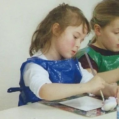 Two young girls painting cermaic animals at a table, wearing smocks for an art activity.