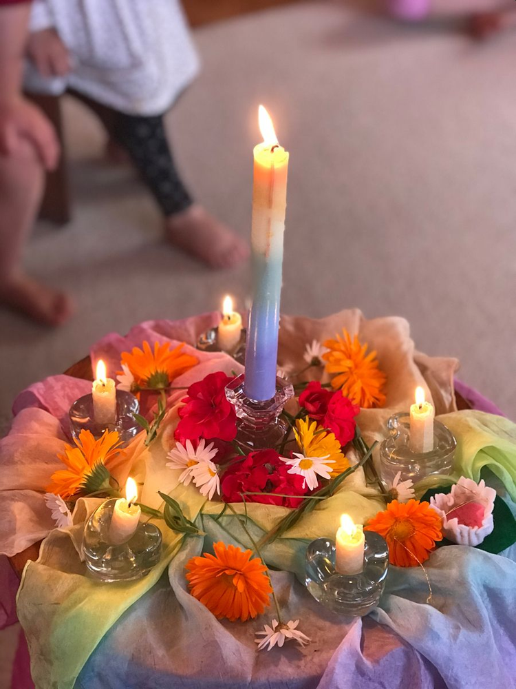 Decorative table centerpiece with candles and colorful flowers on multicolored cloth.