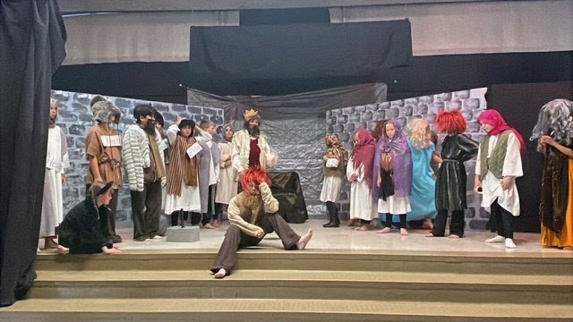 Children dressed as characters performing on stage in a school play with castle walls backdrop.