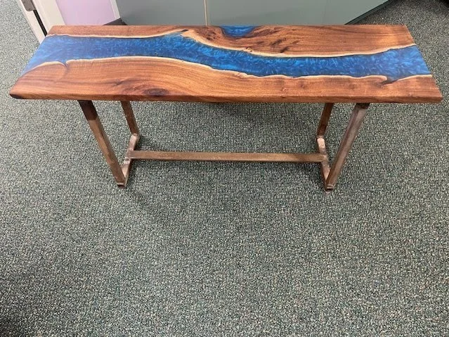 Wooden table with a blue resin river running through the top, placed on a carpeted floor.