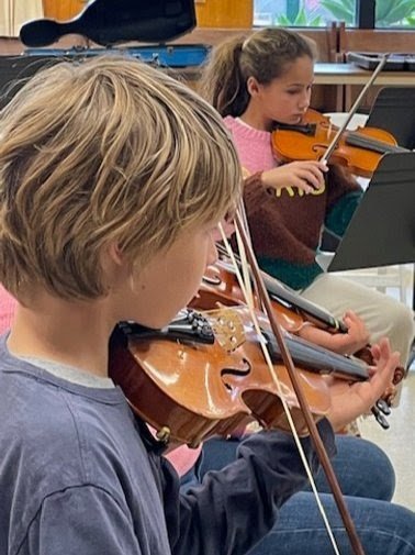 Two children playing violins in a classroom.