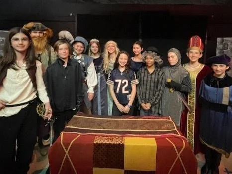 Group of people dressed in historical and cultural costumes standing behind a decorated table.