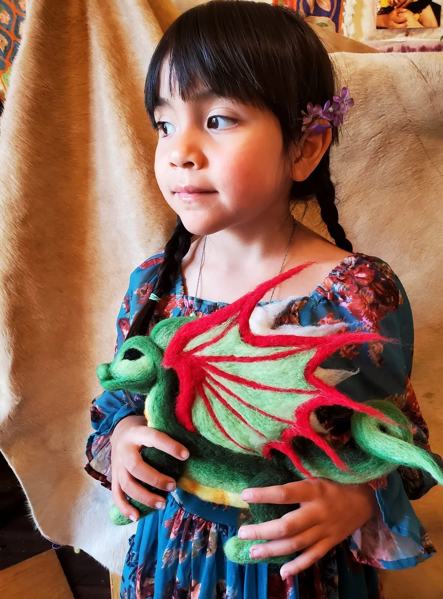 A young girl with black hair holding a colorful felt dragon toy.