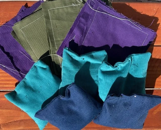 A pile of folded fabric and cloth pieces in purple, green, teal, and navy blue on a wooden surface.