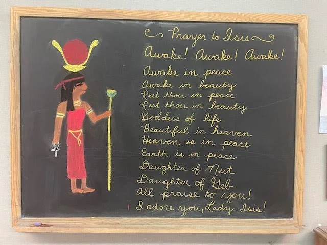 Chalkboard with a drawing of a woman dressed as a goddess, wearing a crown, holding a scepter and an ankh, with a written prayer to Jesus and decorative text.