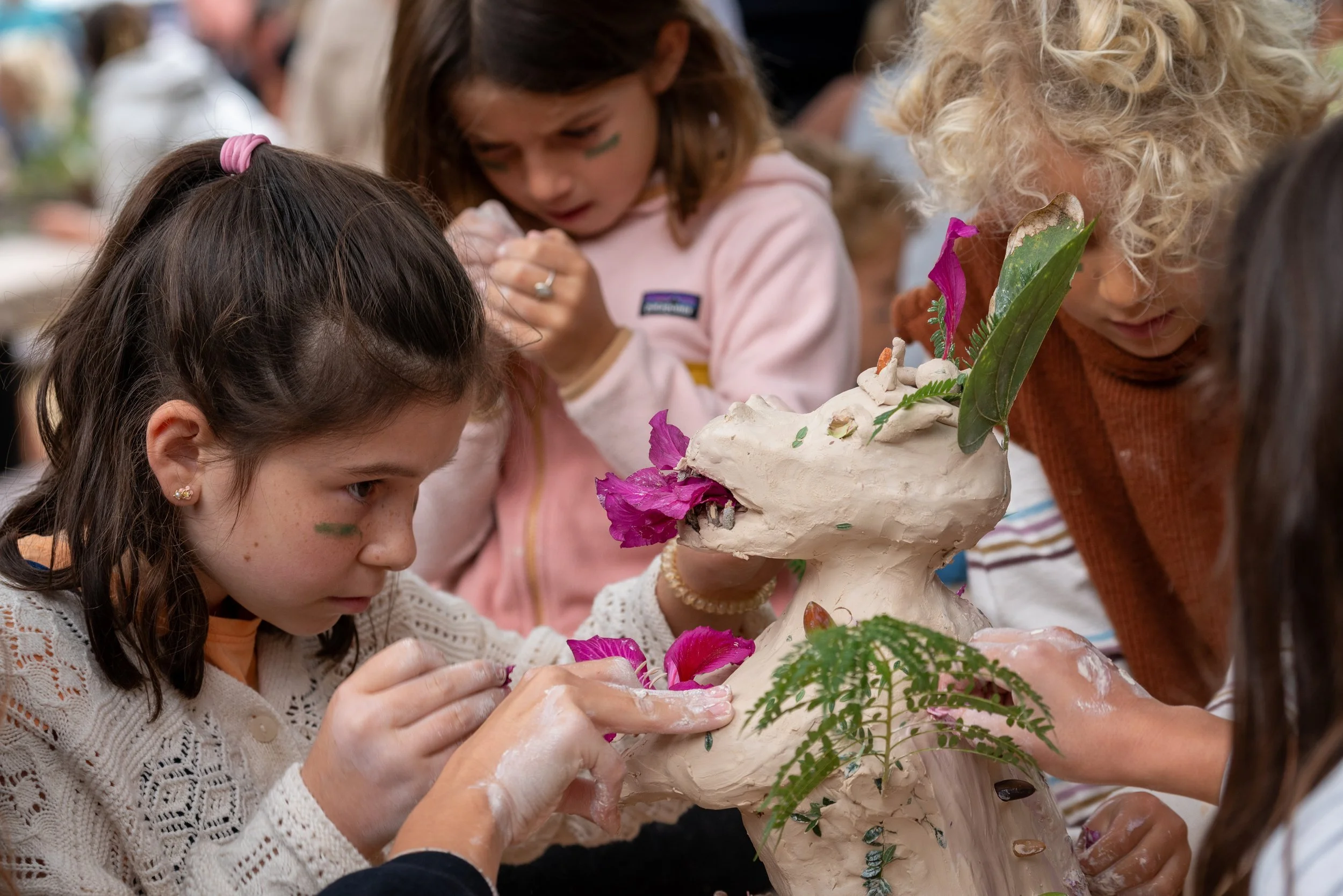 Children decorating a sculpture with flowers, leaves, and paint during an art activity.