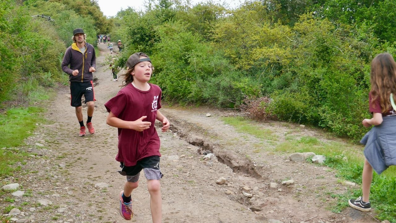 Children running on a dirt trail in a wooded park during the day.