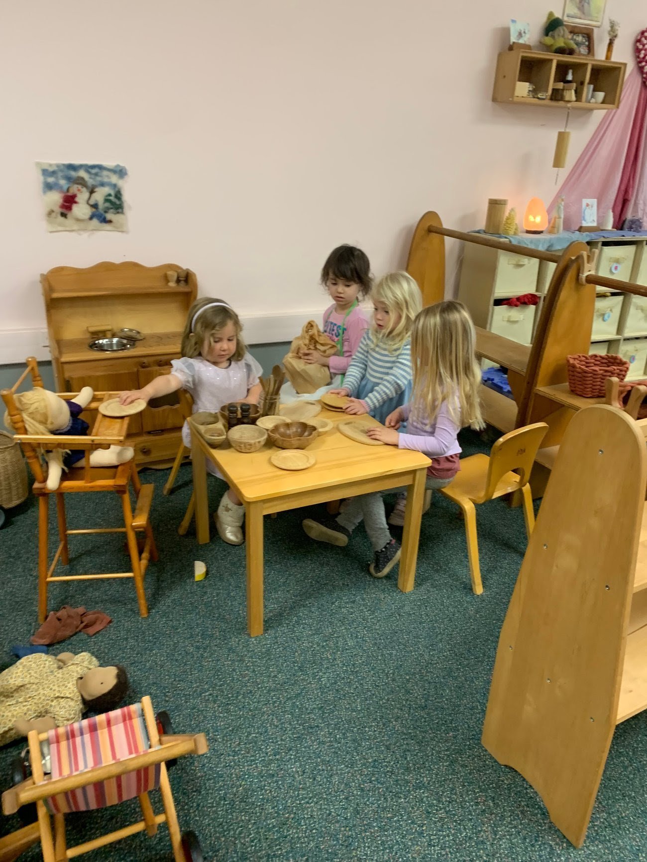 Five young girls playing with toy kitchen bowls and wooden dishes in a playroom.