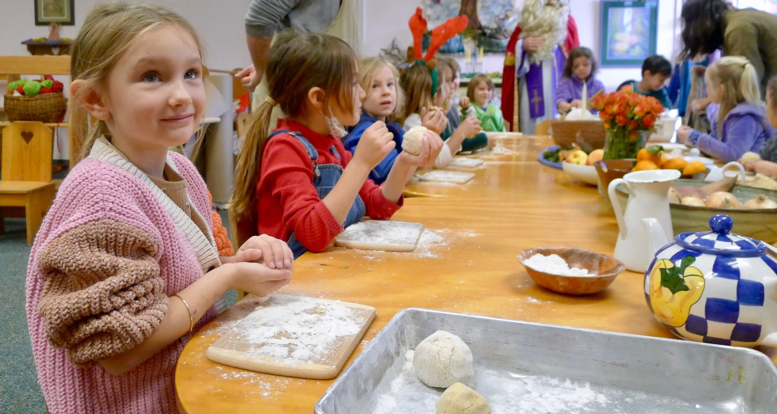 Children participating in a festive cooking activity, with some wearing reindeer antlers, in a decorated indoor setting.