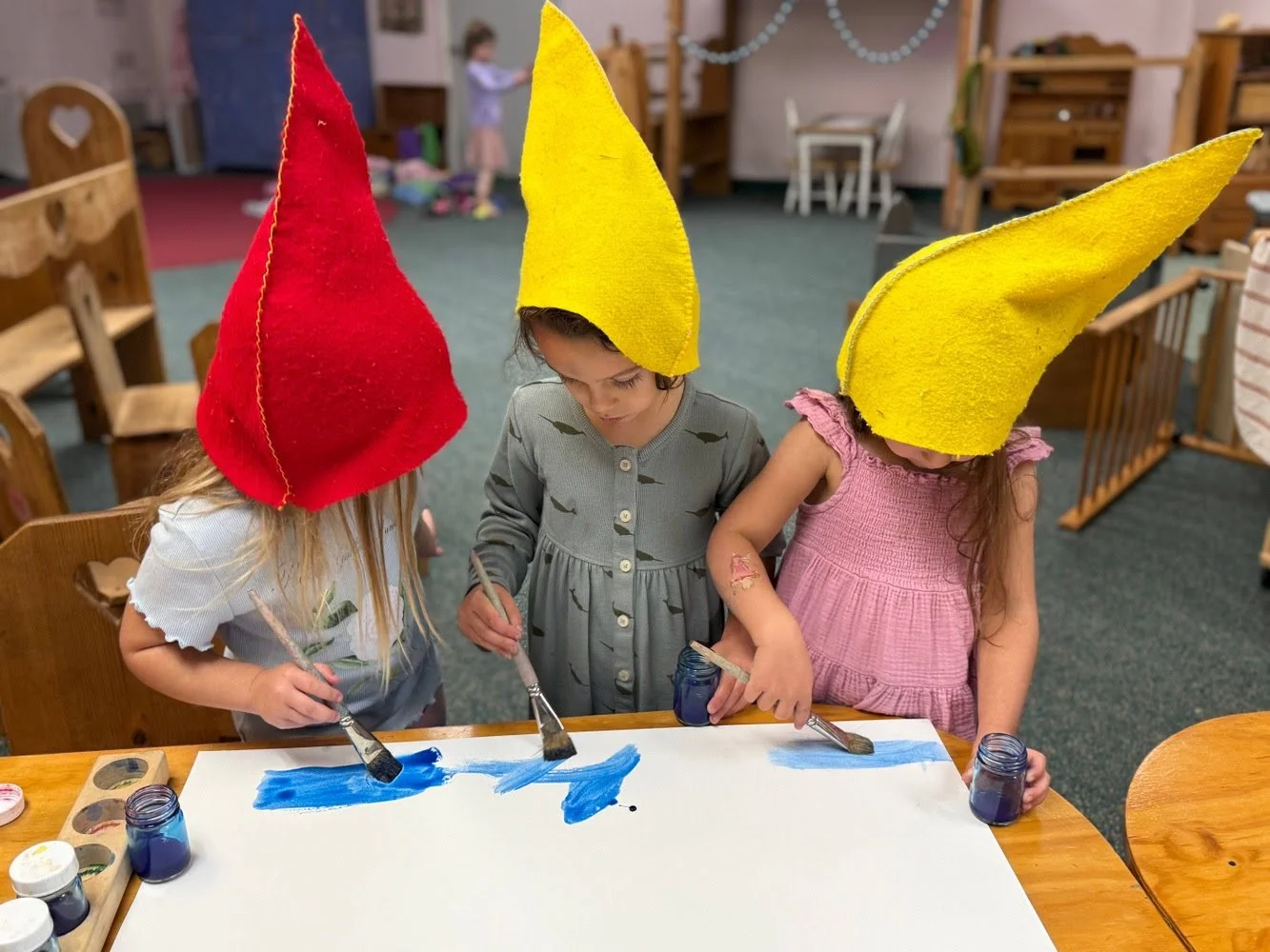 Children wearing colorful clothes and floral headbands holding hands and dancing in a circle outdoors on a grassy field during a sunny day.