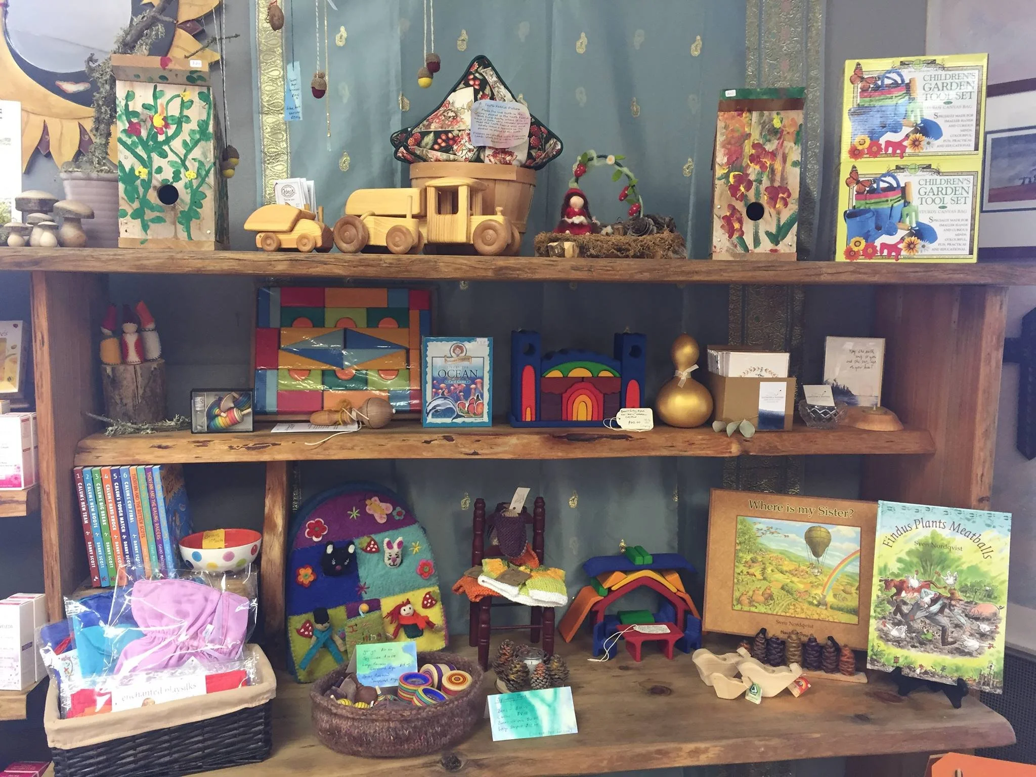 Display shelf with children’s toys and books, including wooden figures, craft kits, picture books, and decorative items.
