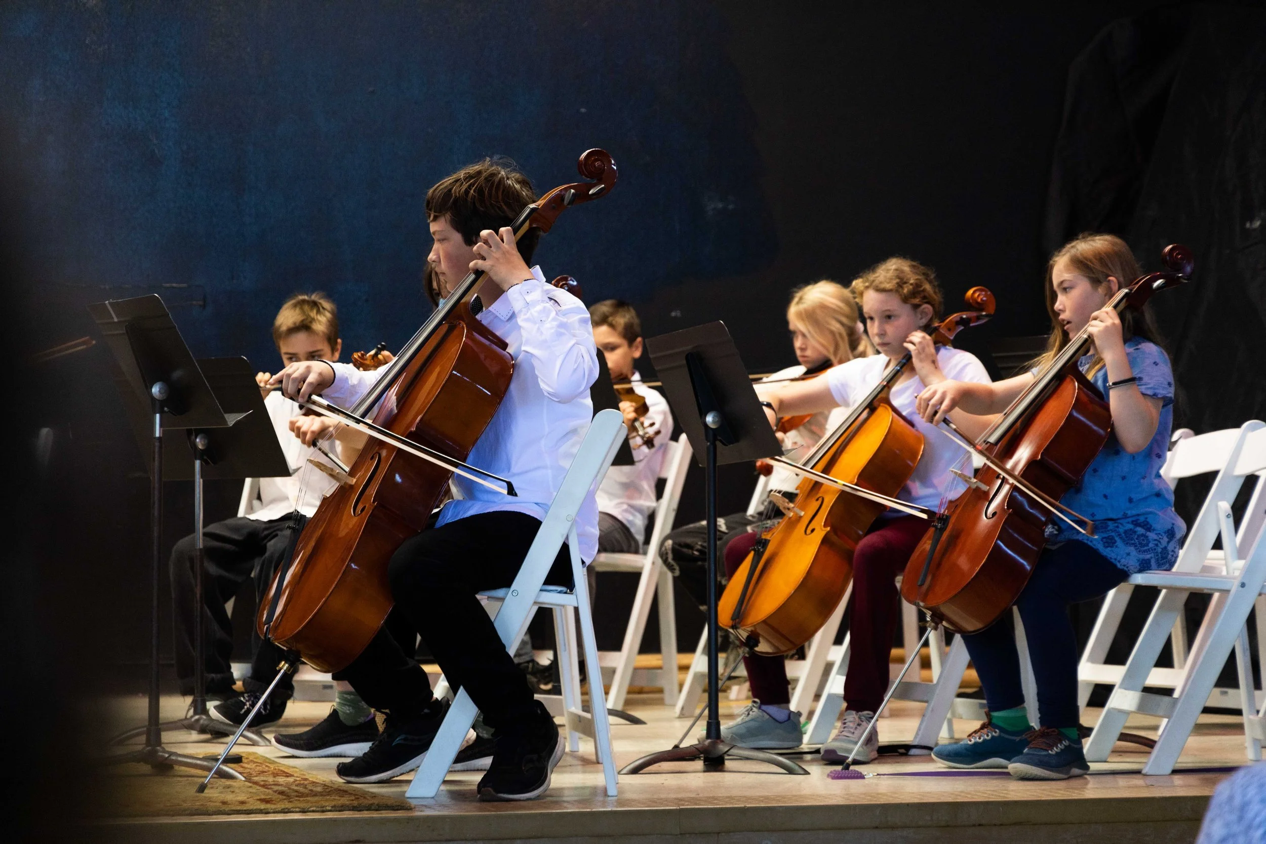 Children playing cellos during a concert in a concert hall.