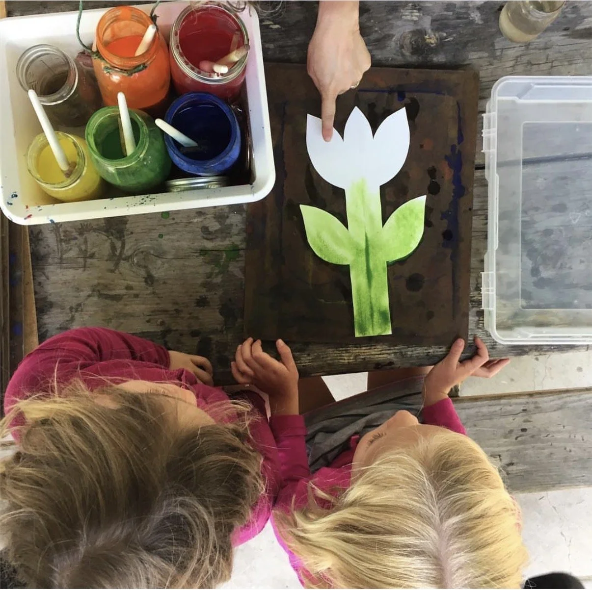Children performing a nativity play on stage with painted desert background and palm tree, dressed in biblical costumes, in front of an audience.